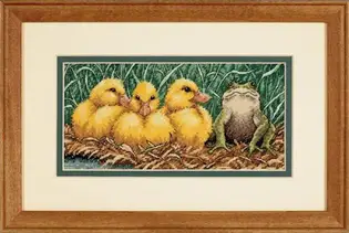 отова вишита картина за набором Dimensions 65094 "Ugly Duckling" (Гидке каченя). Три яскраво-жовтих пухнастих каченяти та кумедна зелена жаба з поважним виглядом сидять у гнізді на тлі густої трави, вишиті технікою лічильного хреста на дрібній канві Aida 18 кольору слонової кістки
