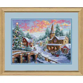 Готова вишита картина хрестиком за набором Dimensions 08783 "Holiday Village" (Святкове село). Казковий зимовий пейзаж із засніженим містечком, великою прикрашеною різдвяною ялинкою, кам'яним містком та церквою на тлі яскравого рожевого заходу сонця у горах