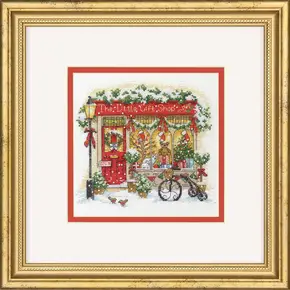 Готова вишита картина хрестиком за набором Dimensions 70-09623 "The Little Gift Shop" (Маленький подарунковий магазин). Затишна зимова вітрина європейської крамнички з червоними дверима, різдвяним вінком, ошатною ялинкою та іграшками. Поруч стоїть засніжений ретро-велосипед під теплим світлом ліхтаря.